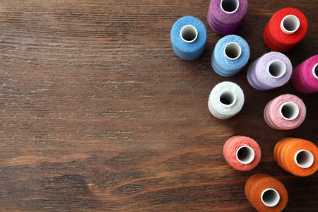 Set of colorful sewing threads on wooden table, flat lay. Space for text