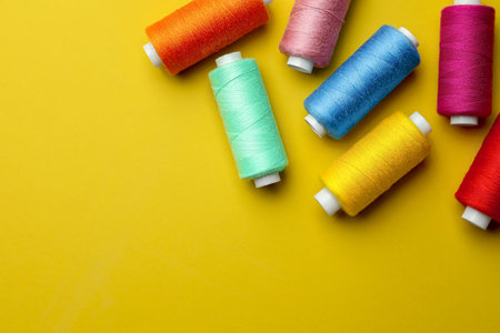 Different colorful sewing threads on yellow background, flat lay. Space for textの写真素材