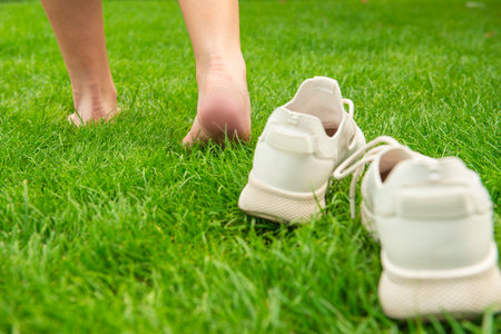 Woman leaving her sneakers and walking away barefoot on green grass, closeupの写真素材