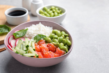 Poke bowl with salmon, edamame beans and vegetables on light gray table, space for text
