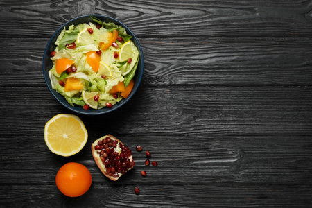 Delicious salad with Chinese cabbage, lemon, persimmon and pomegranate seeds on black wooden table, flat lay. Space for textの写真素材