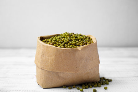 Paper bag with green mung beans on white wooden tableの写真素材