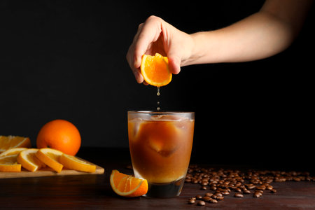 Woman squeezing orange juice into glass of refreshing drink with coffee at wooden table, closeupの写真素材