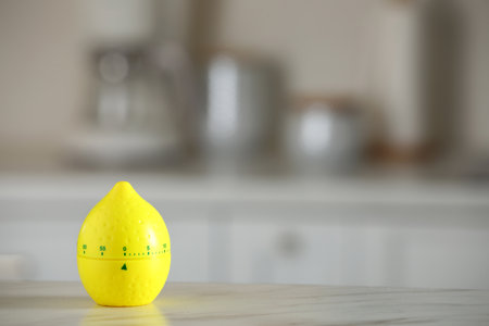 Kitchen timer in shape of lemon on white marble table against blurred background. Space for textの写真素材