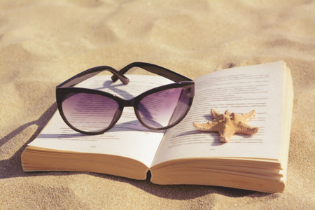 Beautiful sunglasses, book and starfish on sand, closeupの写真素材