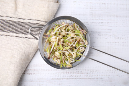 Mung bean sprouts in strainer and kitchen towel on white wooden table, top viewの写真素材