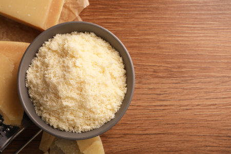 Delicious grated parmesan cheese in bowl on wooden table, flat lay. Space for textの写真素材