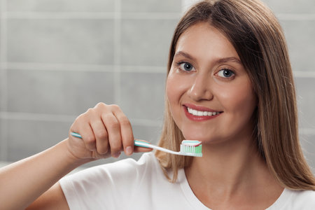 Young woman holding brush with toothpaste in bathroomの写真素材