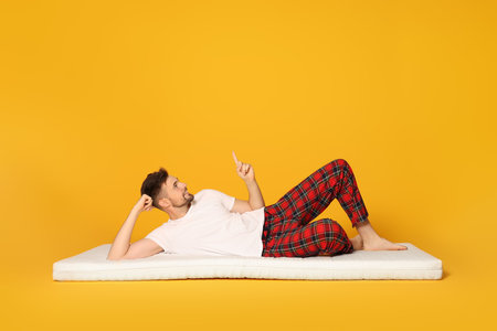 Man on soft mattress pointing upwards against orange backgroundの写真素材