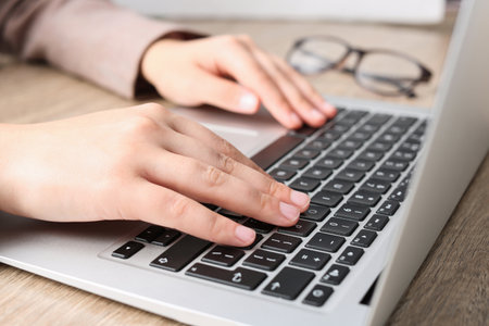 Woman working on laptop at wooden table, closeup