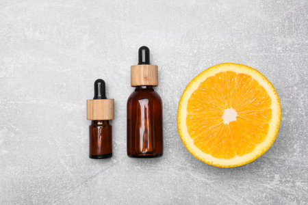 Bottles of essential oil with orange slice on gray table, flat layの写真素材