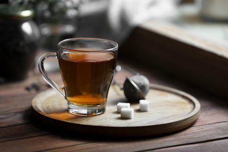 Tray with cup of freshly brewed tea and sugar cubes on wooden table indoorsの写真素材