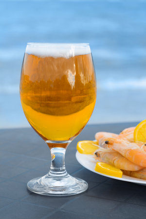 Cold beer in glass and shrimps served with lemon on beach, closeupの写真素材