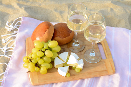 Glasses with white wine and snacks for beach picnic on sand outdoorsの写真素材