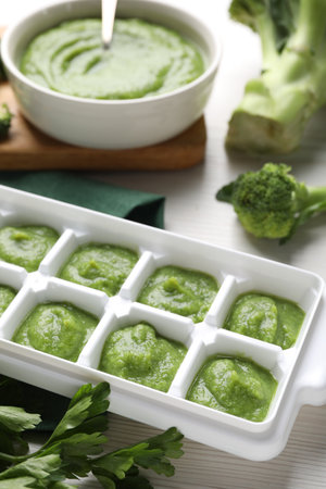 Broccoli puree in ice cube tray and ingredients on white wooden table. Ready for freezingの写真素材