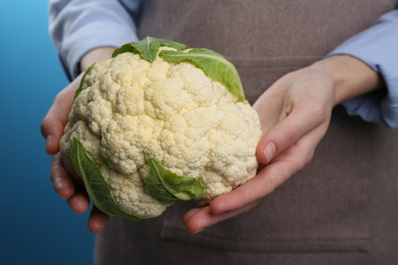 Woman holding fresh cauliflower against blue background, closeupの写真素材