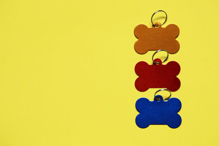 Color metal pet tags on yellow background, flat lay. Space for textの写真素材