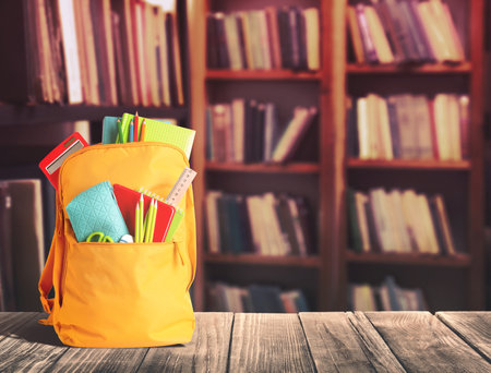 Backpack with school stationery on wooden table in library, space for textの写真素材