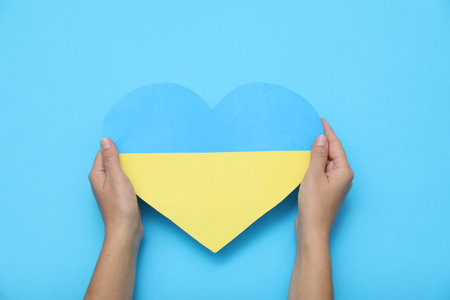 Woman holding paper heart in colors of Ukrainian flag on light blue background, top viewの写真素材
