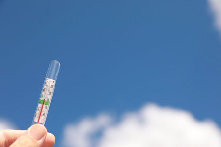 Woman holding weather thermometer against blue sky, closeup. Space for text