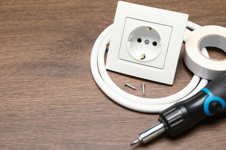 Power socket, screwdriver, cable and insulating tape on wooden table. Space for text