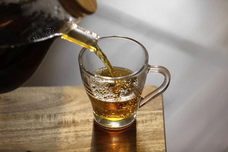 Pouring delicious tea into glass cup on wooden table, closeup