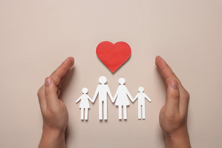 Man protecting paper family figures and red heart on beige background, top view. insurance conceptの写真素材
