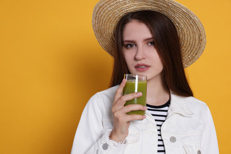 Beautiful young woman with glass of juice on yellow background. Space for textの写真素材