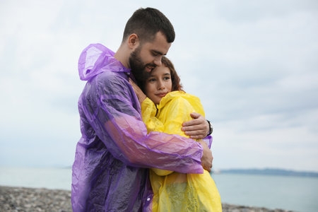 Young couple in raincoats enjoying time together under rain on beach