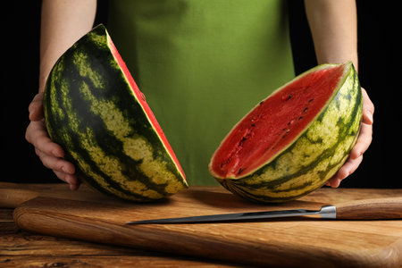 Woman with delicious halved watermelon on wooden table against black background, closeupの写真素材