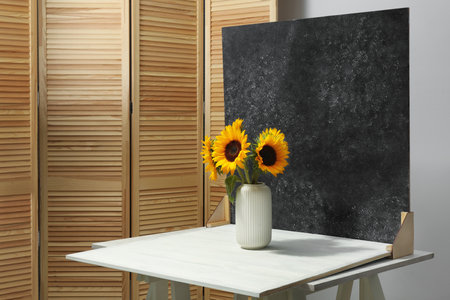 Vase with beautiful sunflowers and double-sided backdrop on table in photo studioの写真素材