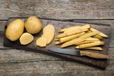 Whole and cut potatoes with knife on wooden table, top view. Cooking delicious french friesの写真素材