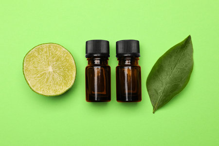 Bottles of citrus essential oil, fresh lime and leaf on green background, flat layの写真素材