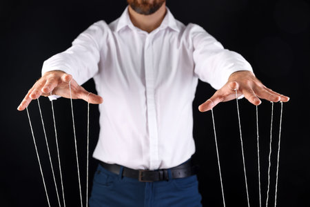 Man in formal outfit pulling strings of puppet on black background, closeupの写真素材