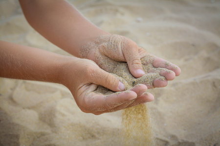 Child pouring sand from hands on beach, closeup. Fleeting time conceptの写真素材