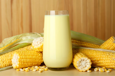 Tasty fresh corn milk in glass and cobs on wooden tableの写真素材