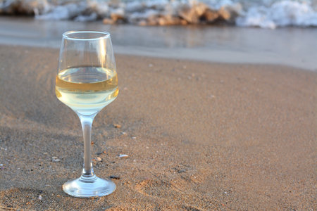 Glass of tasty wine on sand near sea, space for textの写真素材