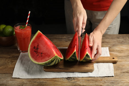 Woman cutting delicious watermelon on wooden table against dark background, closeupの写真素材