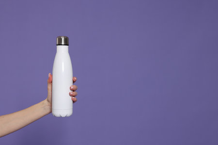 Woman holding thermo bottle on purple background, closeup. Space for textの写真素材