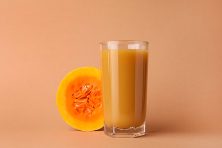 Tasty pumpkin juice in glass and cut pumpkin on pale orange backgroundの写真素材