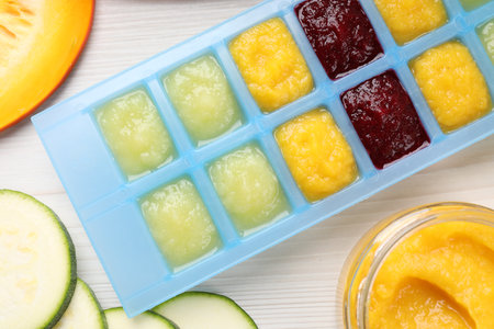 Different purees in ice cube tray and ingredients on white table, flat lay. Ready for freezingの写真素材