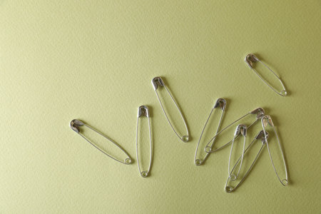 Safety pins on green background, flat lay. Space for text