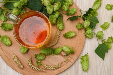 Mug with beer, fresh hops and ears of wheat on light wooden table, flat lay