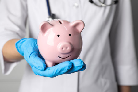 Doctor holding pale pink ceramic piggy bank, closeup. medical insuranceの写真素材