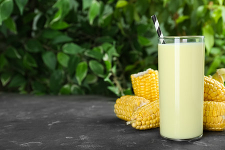 Tasty fresh corn milk and cobs on gray table against blurred background. Space for textの写真素材