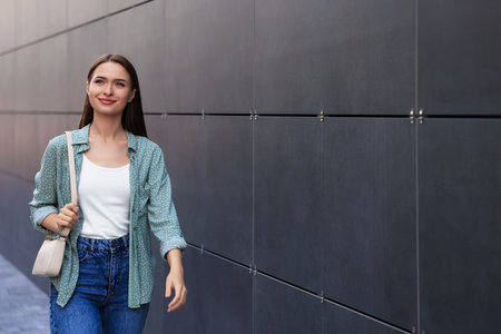 Young woman in casual clothes walking near gray wall outdoors, space for textの写真素材