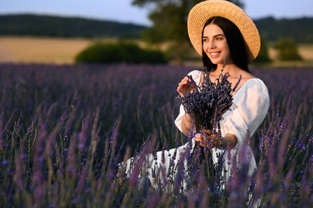 Beautiful young woman with bouquet sitting in lavender fieldの写真素材