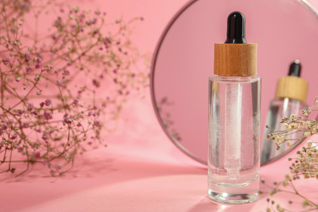 Bottle of face serum and beautiful flowers near mirror on pink background, closeup. Space for textの写真素材