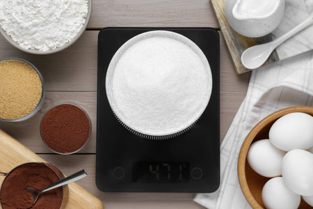 Electronic scales with sugar and different products on light wooden table, flat layの写真素材