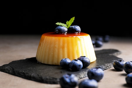 Delicious caramel pudding with blueberries and mint on gray table against black background, closeupの写真素材